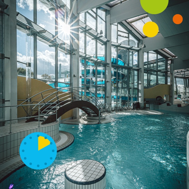 Blick auf das Erlebnisbecken im Triamare mit türkisblauem Wasser, einer kleinen geschwungenen Brücke und großen Glasfenstern, durch die Sonnenlicht in die Schwimmhalle fällt. Unten links zeigt ein blaues Uhrsymbol mit gelbem Segment eine Aufenthaltsdauer
