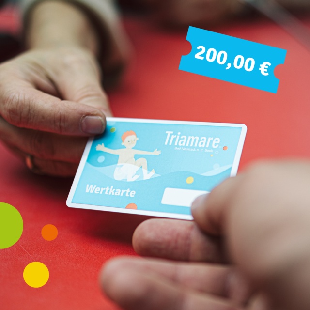 Nahaufnahme einer Triamare-Wertkarte, die zwischen zwei Personen übergeben wird. Auf der Karte steht ‚Wertkarte‘, daneben ist ein blaues Ticket mit dem Wert 20,00 € dargestellt. Das Motiv steht für eine 200-Euro-Wertkarte des Triamare.